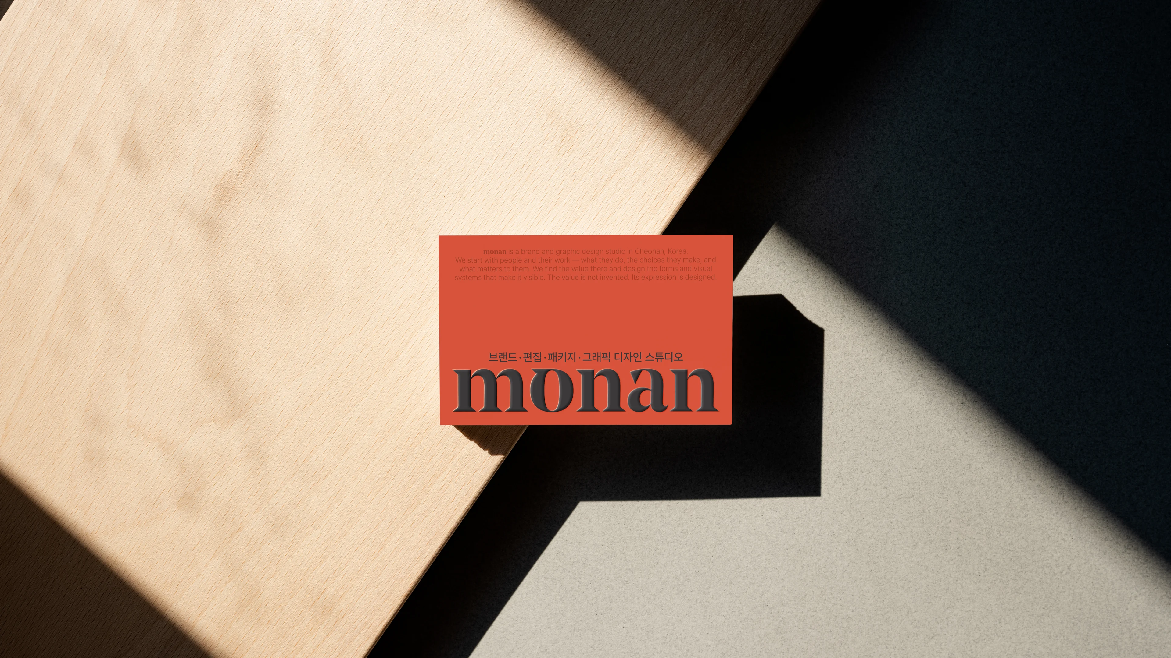 빛과 그림자가 드리운 베이지 면 위의 적색 monan 명함.