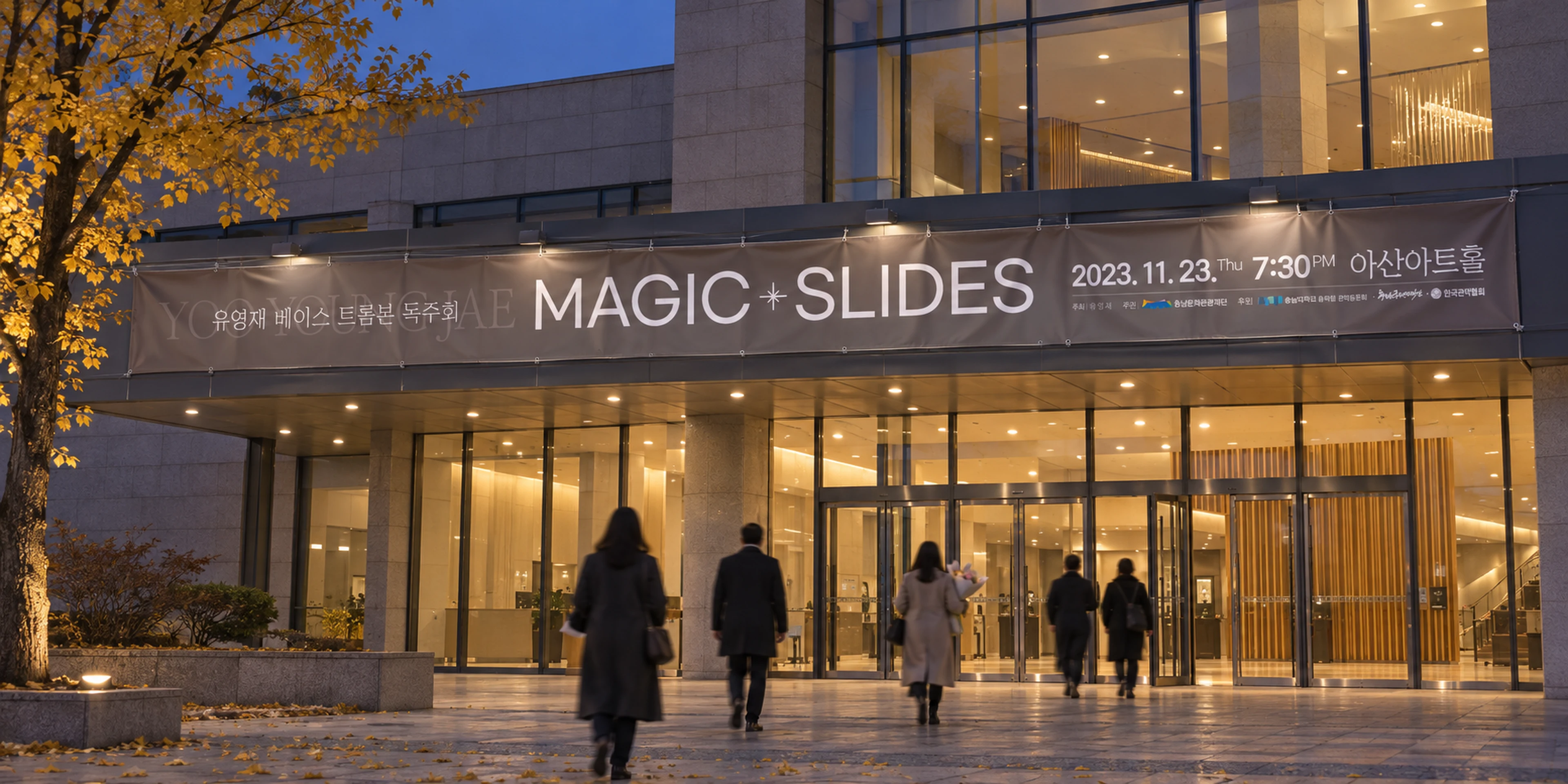 해 질 무렵 공연장 유리 외벽 위에 걸린 MAGIC SLIDES 가로 현수막과 입구로 향하는 관객들.